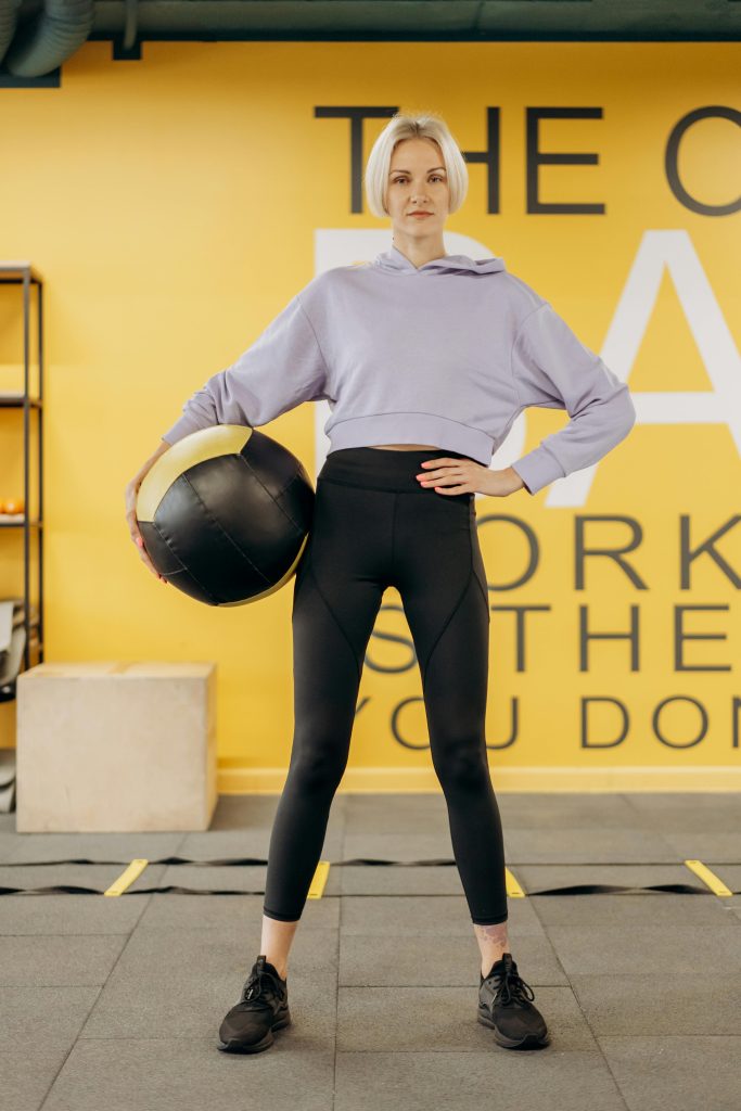 About Us Woman holding a medicine ball in a gym, showcasing strength and focus.